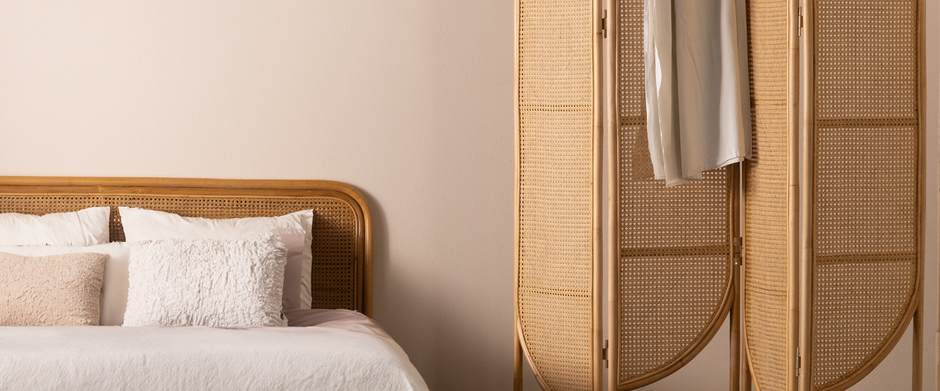 Z lewej strony łóżko z rattanowym zagłówkiem. Po prawej stronie rattanowy parawan ozdobiony plecionką wiedeńską. Na parawanie zawieszona narzuta, a na łóżku ułożone poduszki w miękkiej tkaninie boucele.