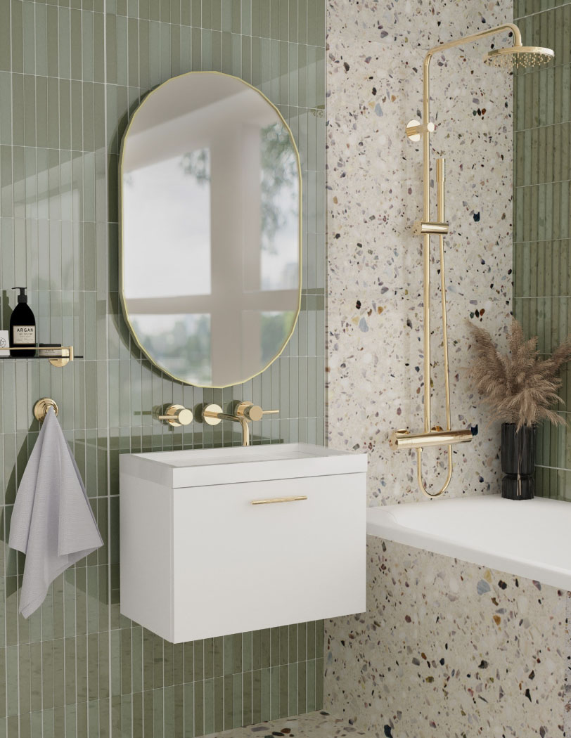 Łazienka z jasnozielonymi płytkami oraz płytkami lastryko. Na ścianie ze złotym lustrem widać wiszącą białą szafkę. Po prawej stronie wanna w zabudowie ze złotym prysznicem.