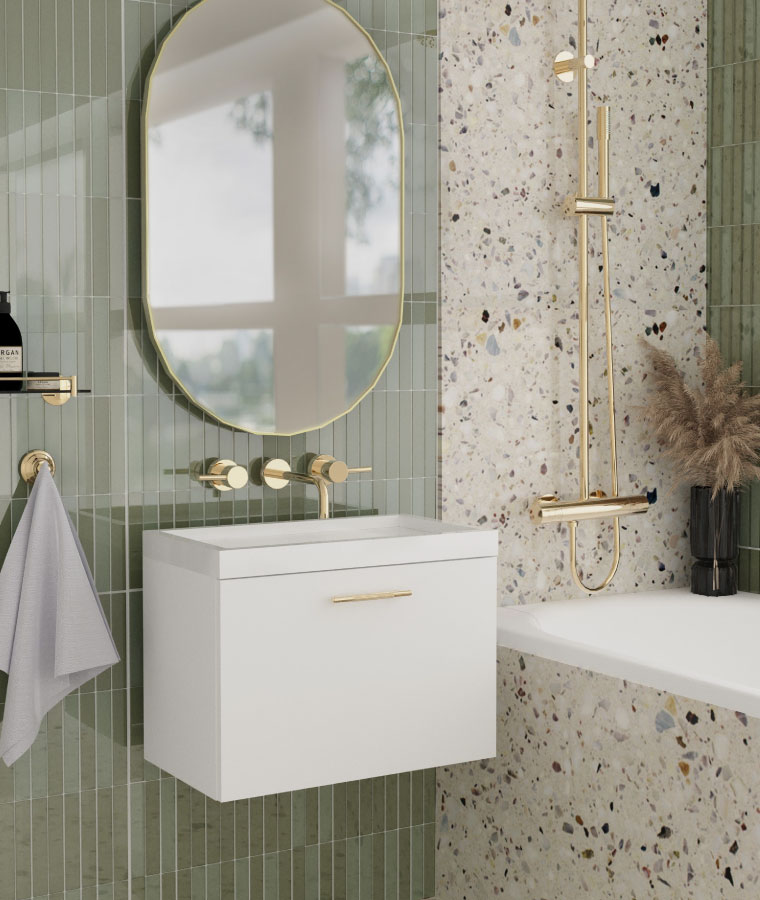 Jasna łazienka w klimacie boho z płytkami w lastryko i z jasnozielonym kolorze. Na jednej ze ścian owalne lustro w złotej ramie i biała umywalka ze złotym uchwytem.