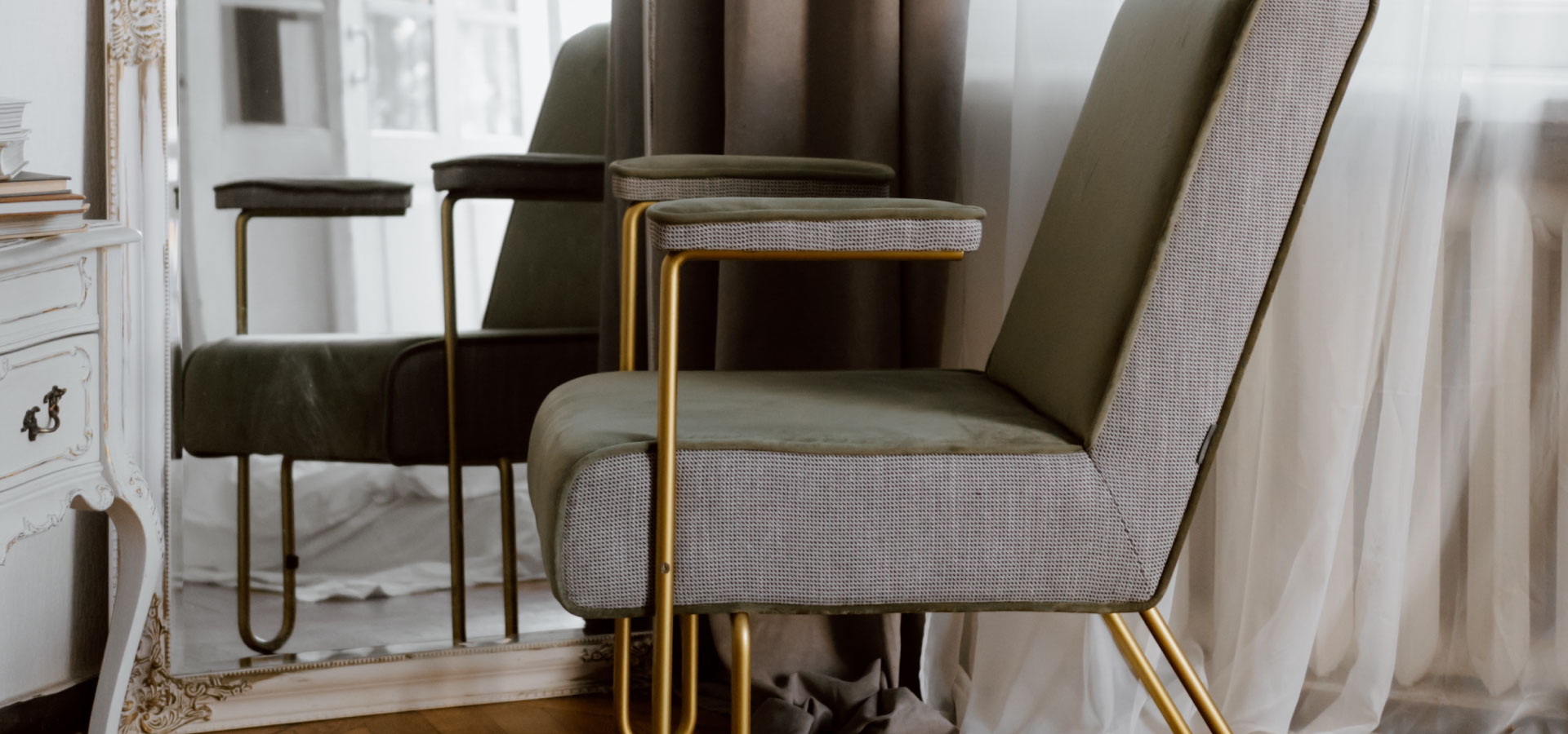 Fragment odnowionego fotela tapicerowanego na złotych nogach. W tle lustro w zdobnej ramie i kawałek szafki w stylu vintage.