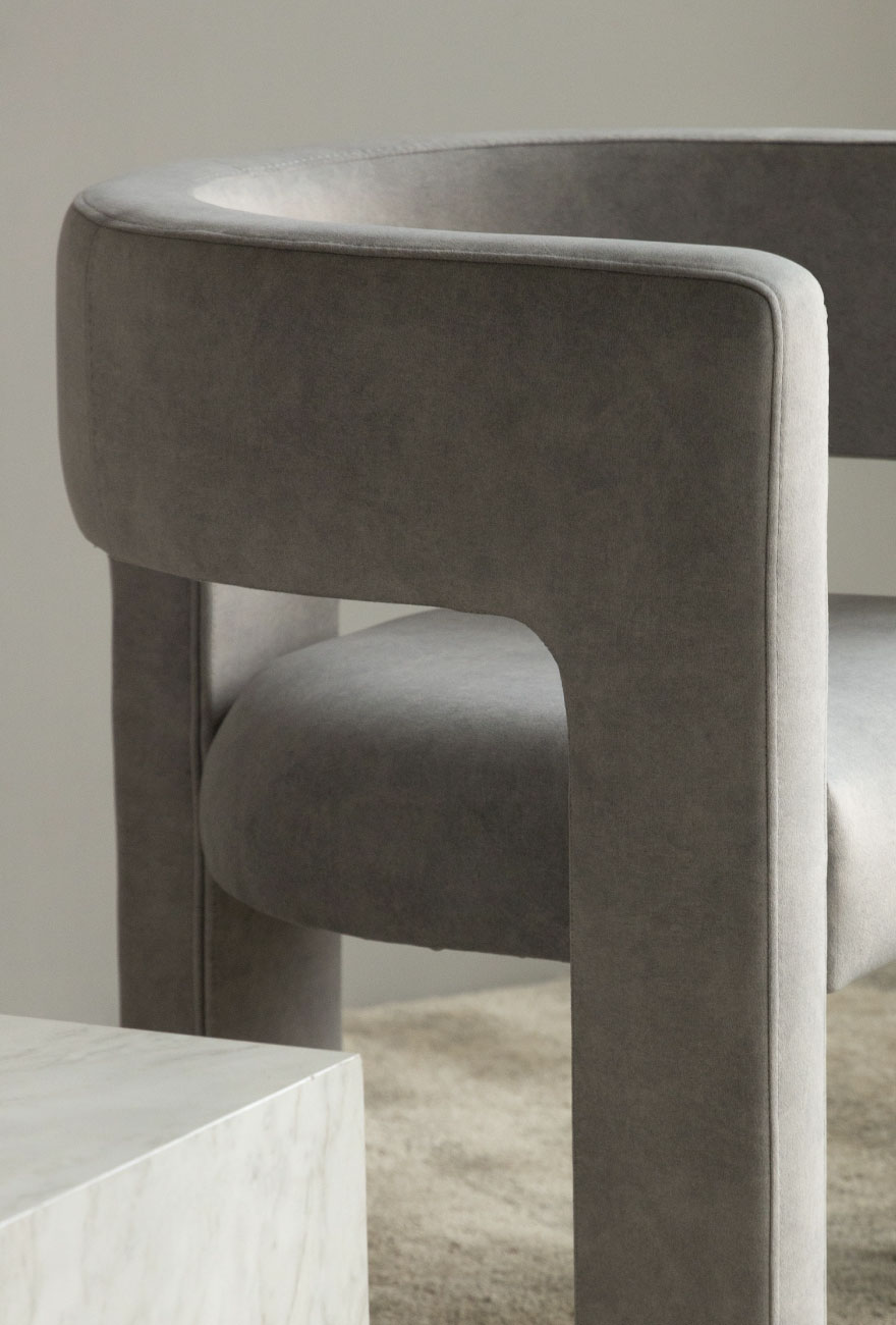 Fragment szarego fotela w designeskim kształcie i na 3 szerokich nogach.