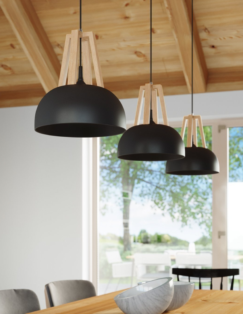 Trzy czarne lampy wiszące z metalowymi kloszami i drewnianą ozdobą nad kloszem. Wszystkie zawieszone nad drewnianym stołem.