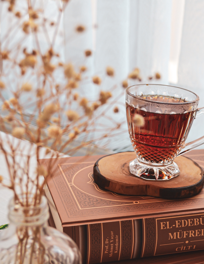 Kubek herbaty w zdobnej szklance, stojący na drewnianej podstawce i książce.