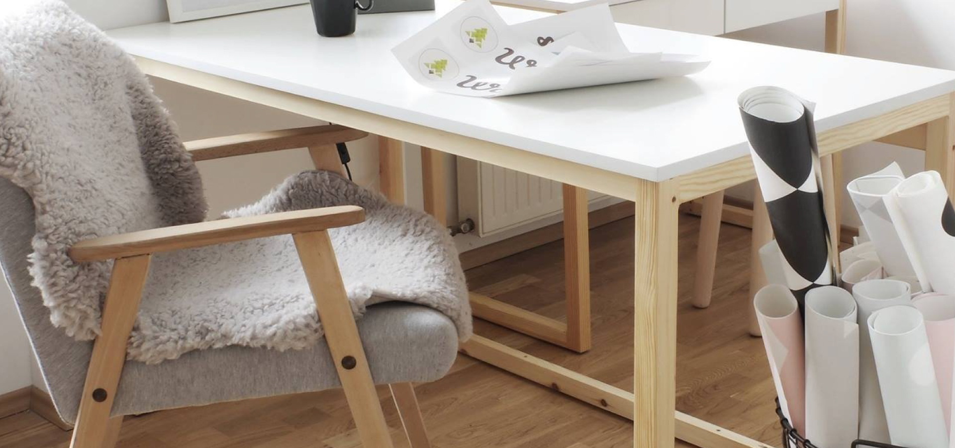 Drewniane łóżko z białym blatem i krzesłem z szarą tapicerką w stylu retro. Na fotelu położony dywanik z owczej skóry.