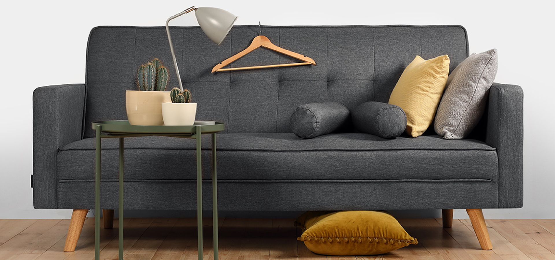 Szara sofa w stylu retro z żółtymi dodatkami i zielonym, wysokim stolikiem kawowym, na którym stoją doniczki z sukulentami.