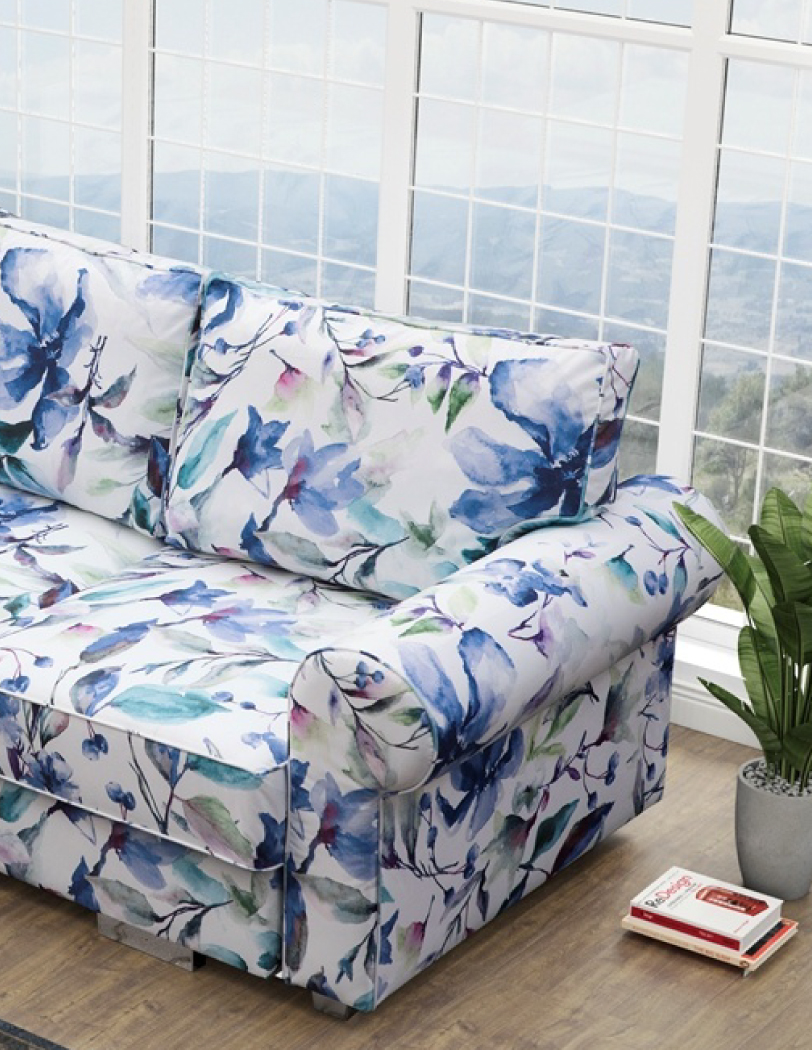 Zbliżenie na bok jasnej kanapy w błękitno-granatowy wzór w kwiaty, cała kanapa w stylu retro, z dużymi poduszkami i szerokimi, zaokrąglonymi podłokietnikami.