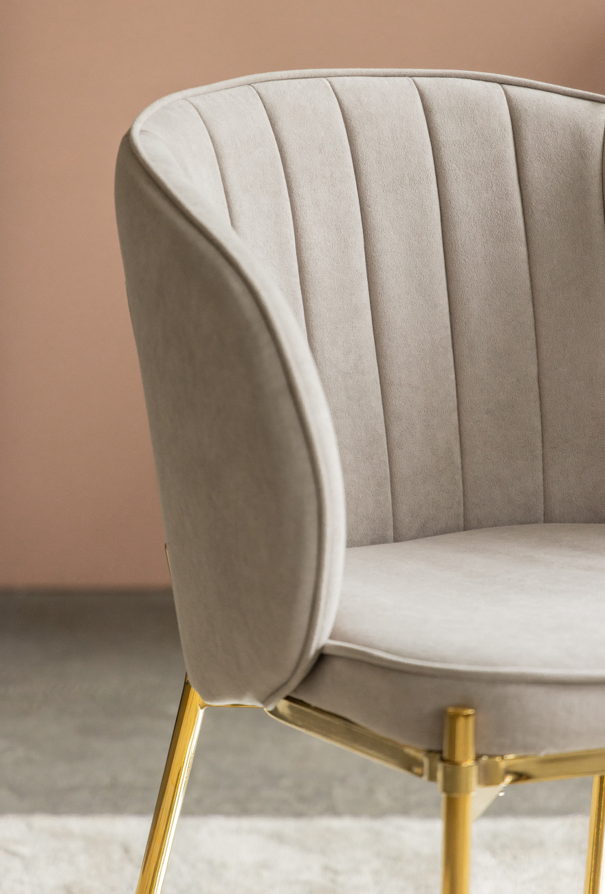 Welurowe krzesło w szarym kolorze z pionowymi przeszyciami na oparciu i złotej konstrukcji.