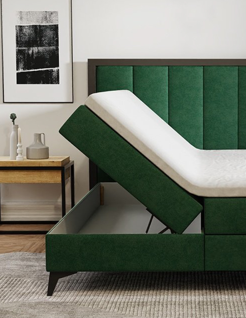 Łóżko kontynentalne w kolorze zielonym z podniesionym bokiem, w tle szafka nocna z ułożonymi dekoracjami.