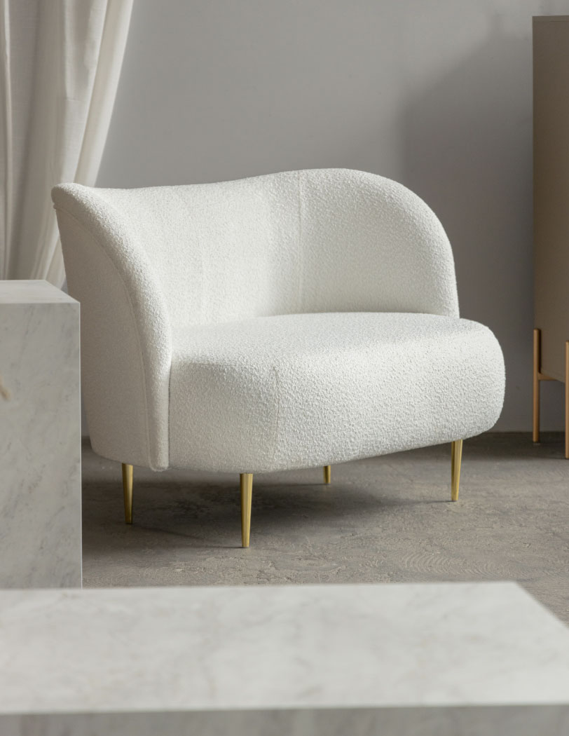 Dwuosobowa sofa w tkaninie boucle i na złotych nóżkach, o obłym kształcie wysokiego oparcia.