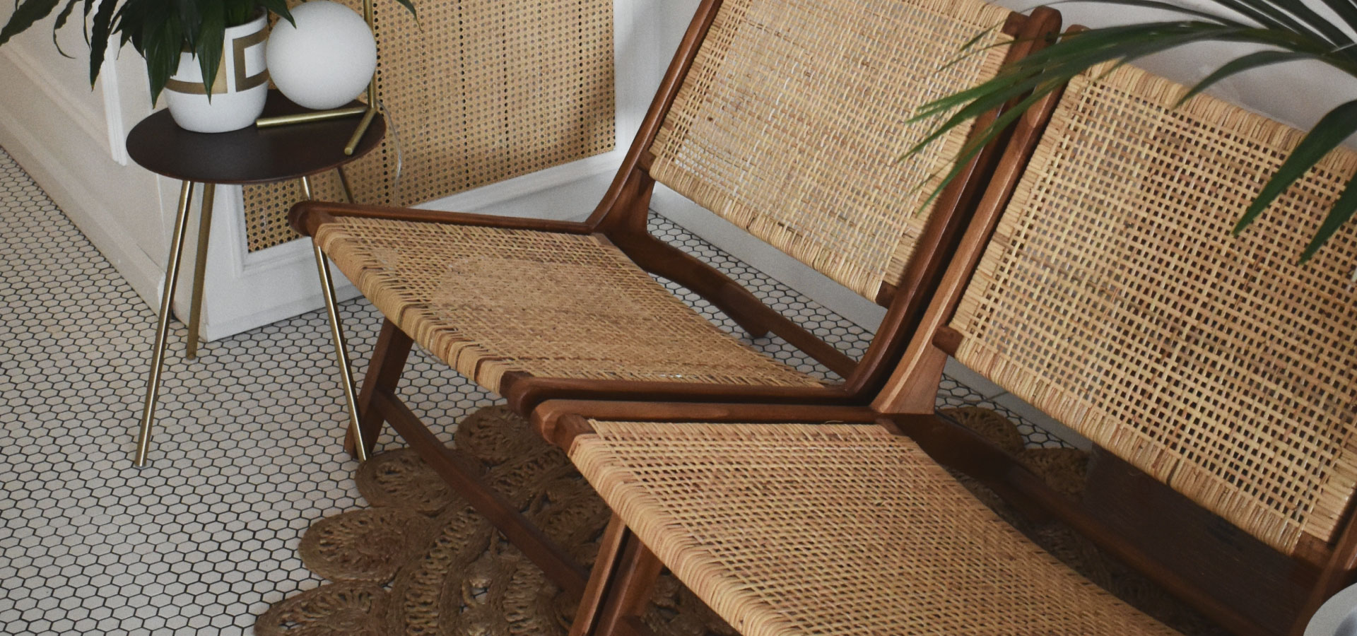 Rattanowe krzesła na drewnianej konstrukcji, w tle niski stolik na złotych nóżkach.