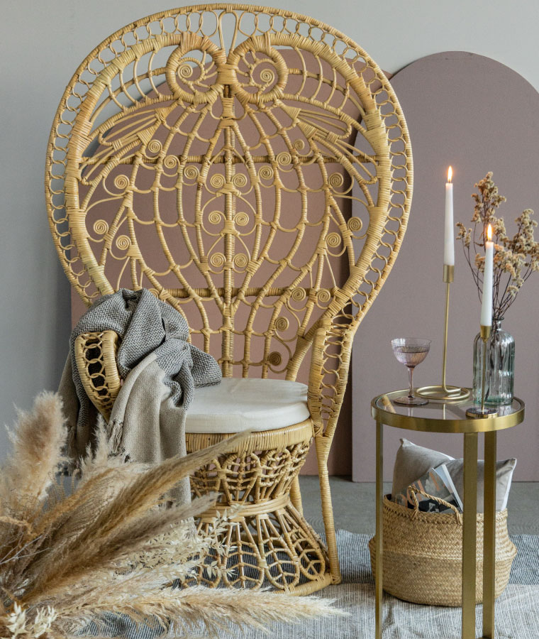 Wysoki tron z rattanu ze zdobnym oparciem i beżowym siedziskiem, obok którego stoi wysoki stolik na złotej konstrukcji.