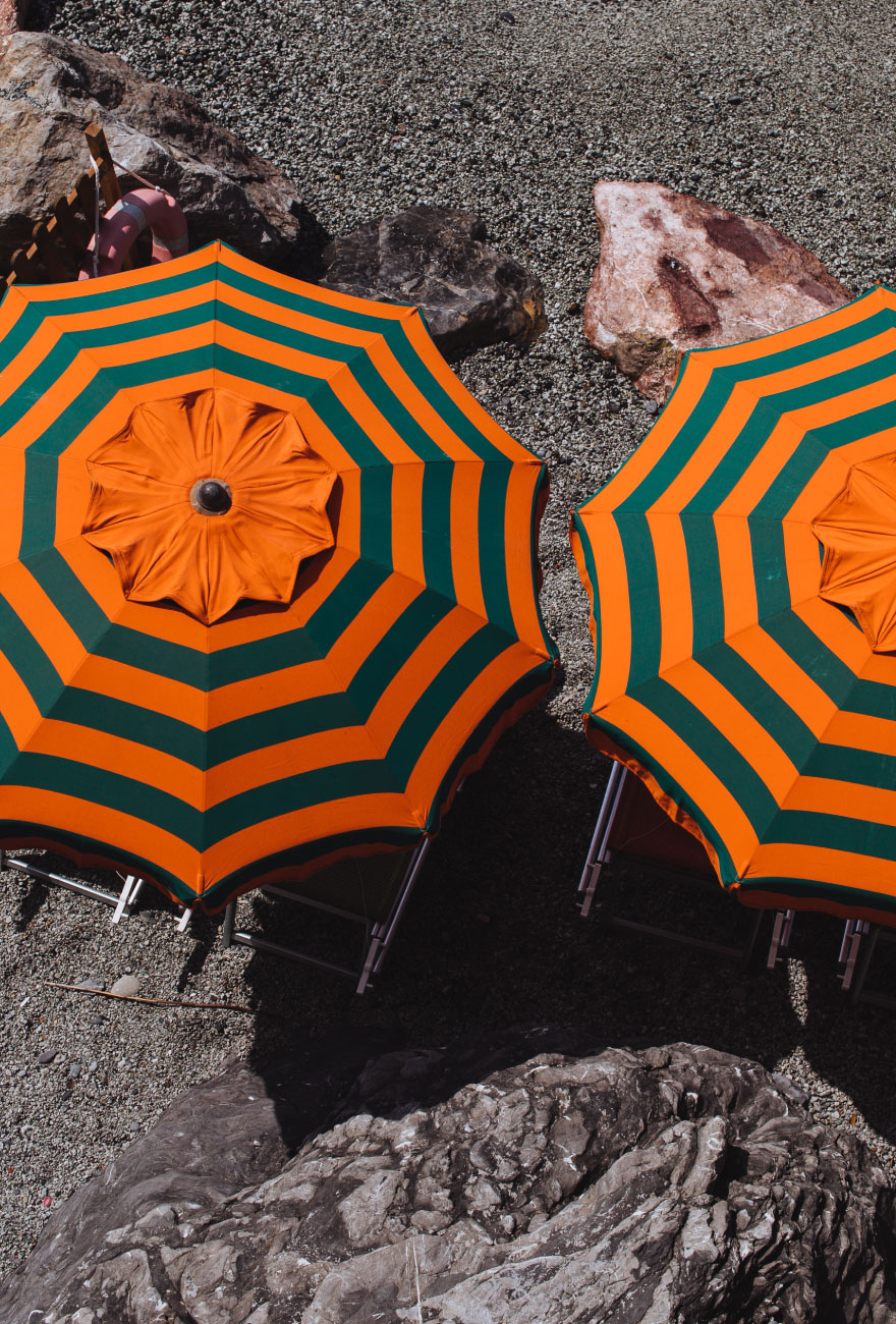 Widok na dwa parasole ogrodowe widoczne od góry z materiałem w zielono-pomarańczowe pasy.