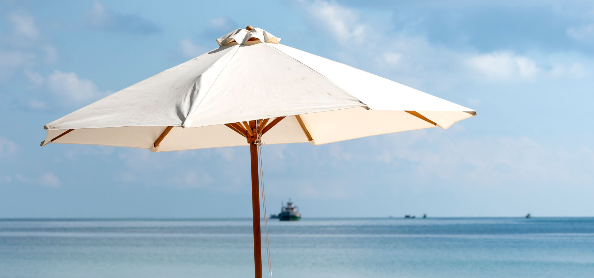 Wysoki beżowy parasol na drewnianej konstrukcji na tle błękitnego nieba i morza.
